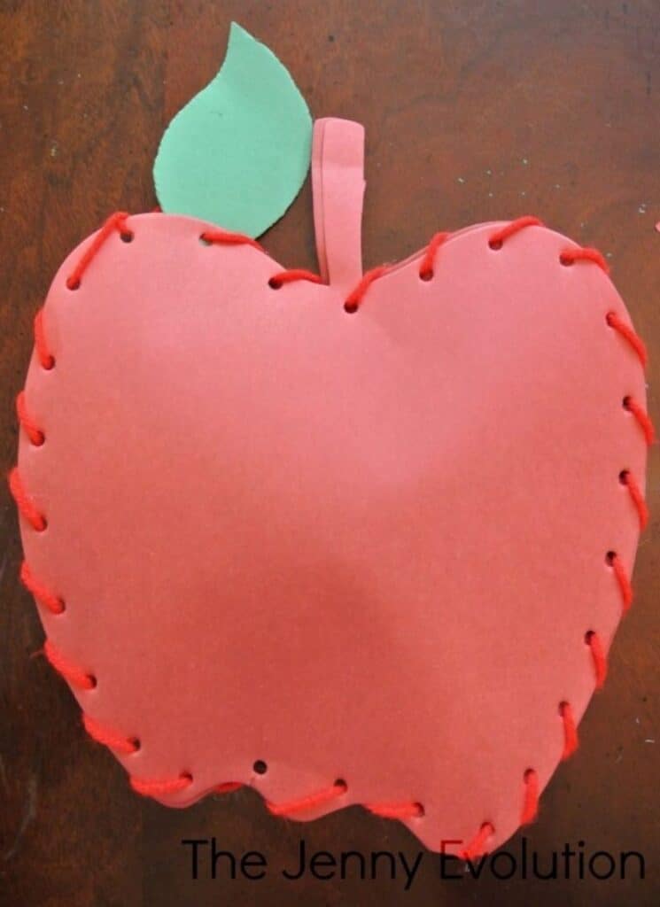 lacing red yarn through pre-punched holes in apple-shaped paper